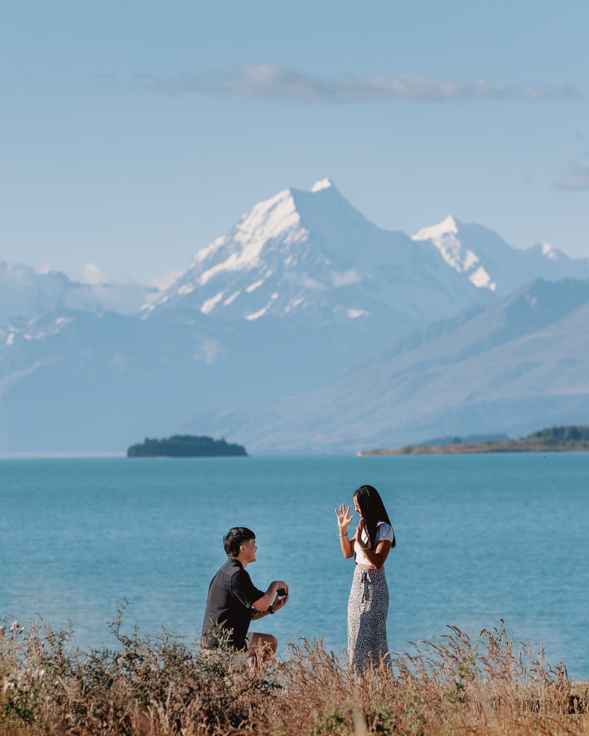Man on one knee proposing to woman during surprise proposal photography at Lake Pukaki with Mt Cook, New Zealand.