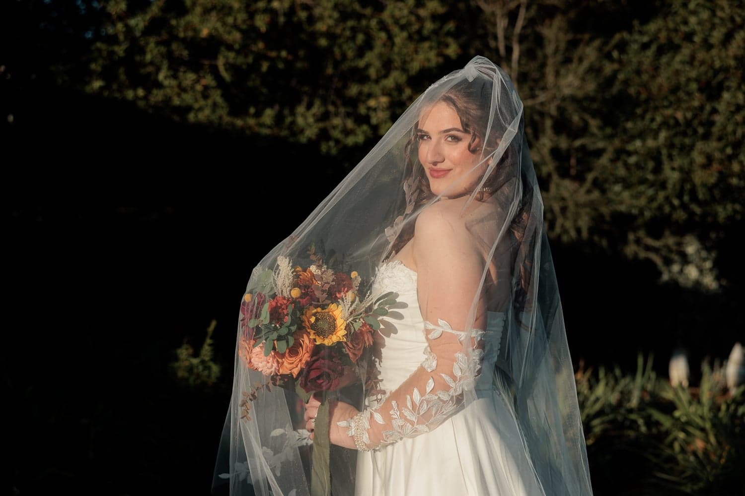 Bride in lace gown holding autumn bouquet under veil, intimate wedding photography in Canberra.