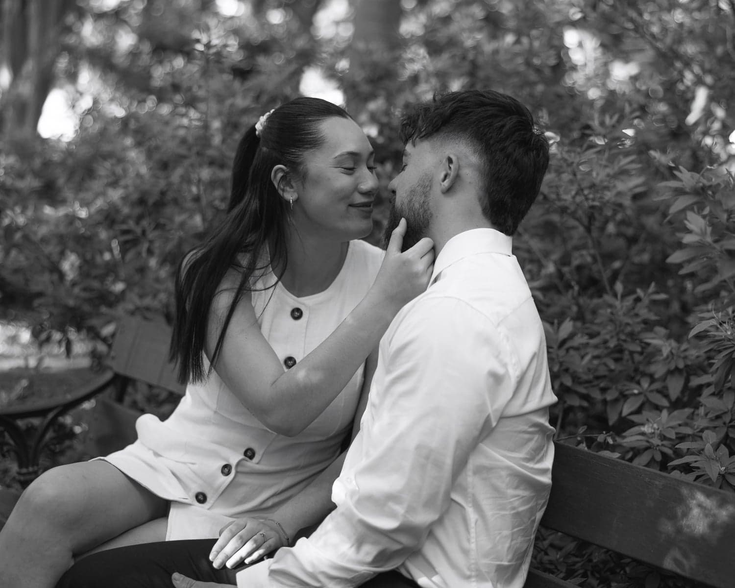 Couple sharing an intimate almost-kiss on a bench during a Canberra engagement shoot, black and white.