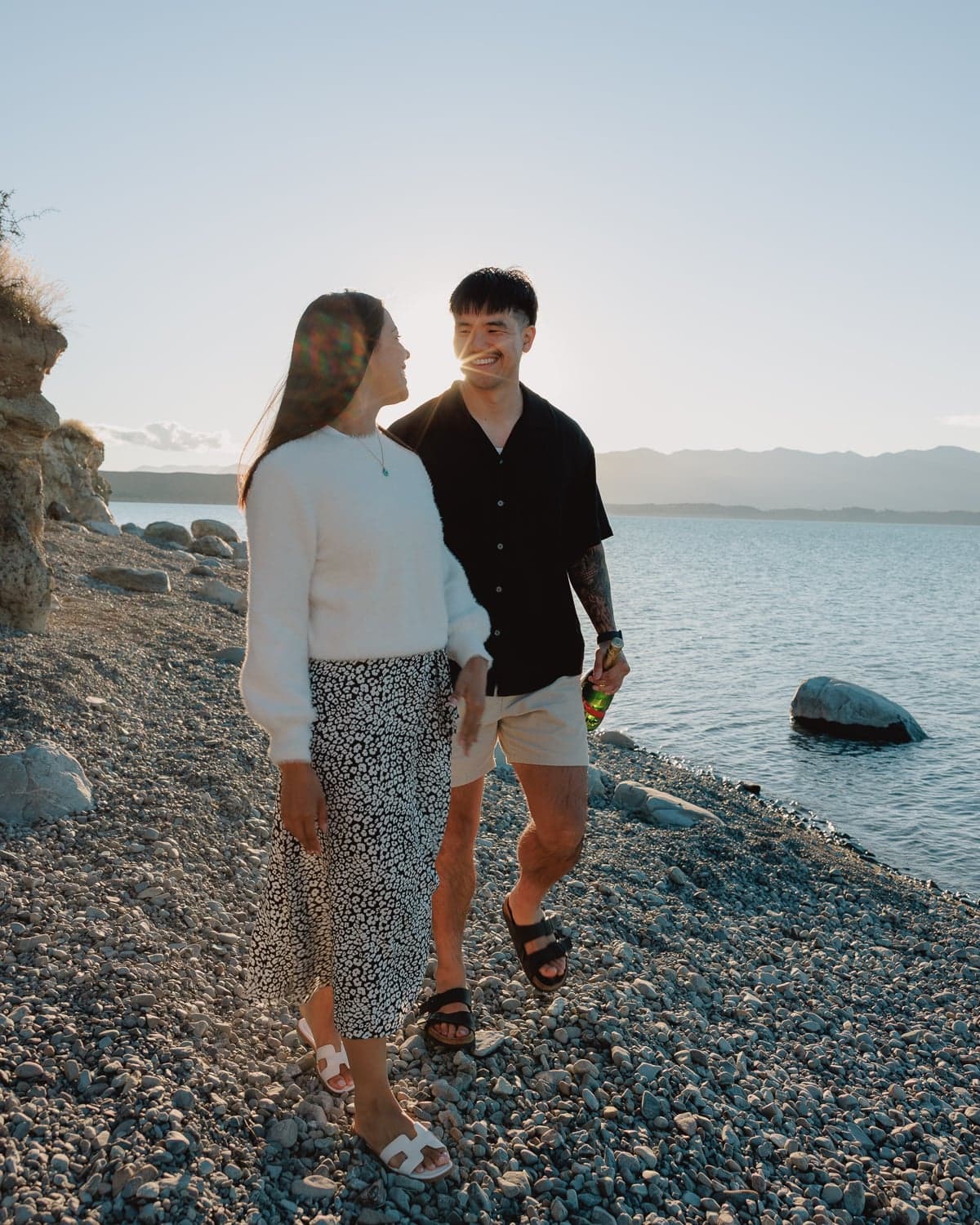 Engaged couple walking along rocky shore during proposal photography at Lake Pukaki, New Zealand, at golden hour.